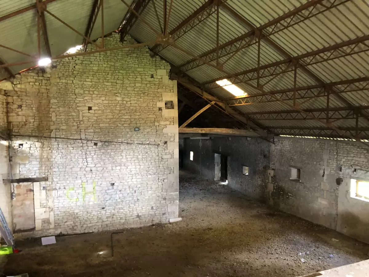 Intérieur de la grande grange en pierre de Saintonge à l'état brut avant rénovation au Domaine des Ânes